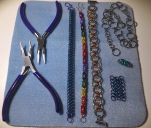 A blue piece of fabric with pliers, three bracelets, and some small hand-made chains on it
