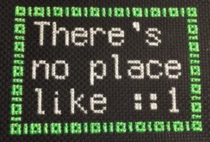 A cross-stitch that says "There's no place like ::1" with 1s and 0s acting as a border