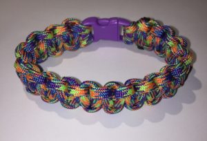 A bracelet made out of brightly colored paracord, with a purple buckle